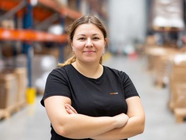 TEAMLOG Mitarbeiterin steht mit verschränkten Armen in einem Lagergang.